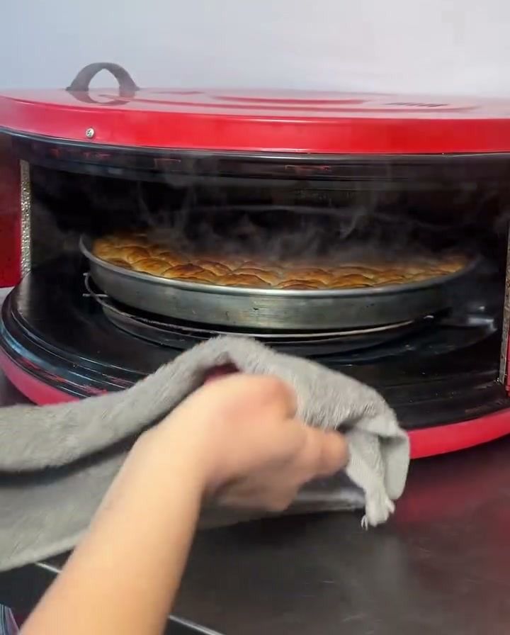 Kırmızı davul fırının kapağı açılıyor, içinden buhar çıkan börek tepsisi görünüyor